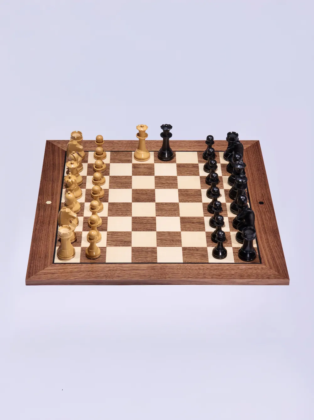 A walnut chess board with the FIDE-approved World Chess pieces set up for the start of a game.